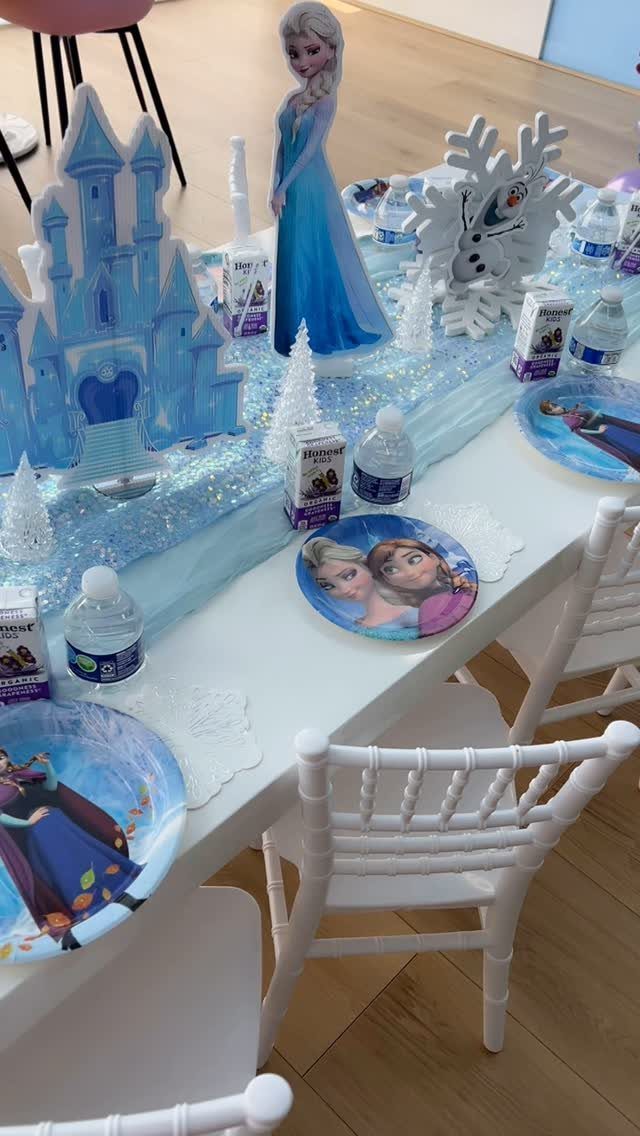 Frozen themed party table setting with Elsa figurine, ice castle, and character plates.