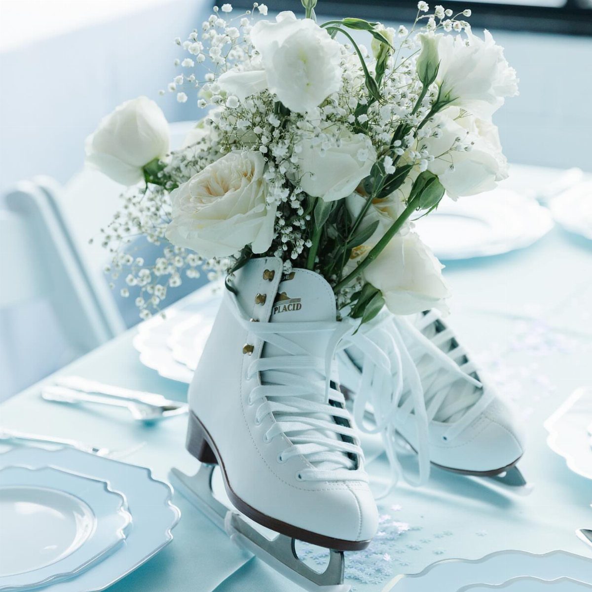 White ice skates holding a bouquet of white roses on a blue table.