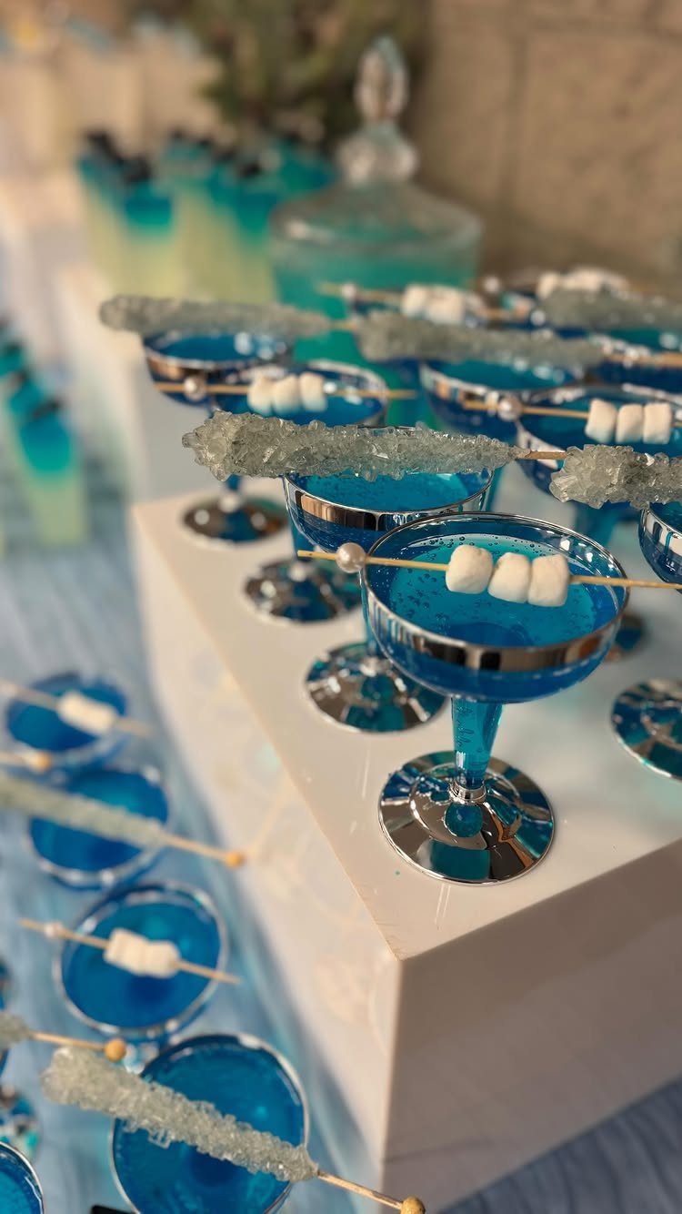 Blue cocktails in martini glasses garnished with marshmallows and blue rock candy sticks.