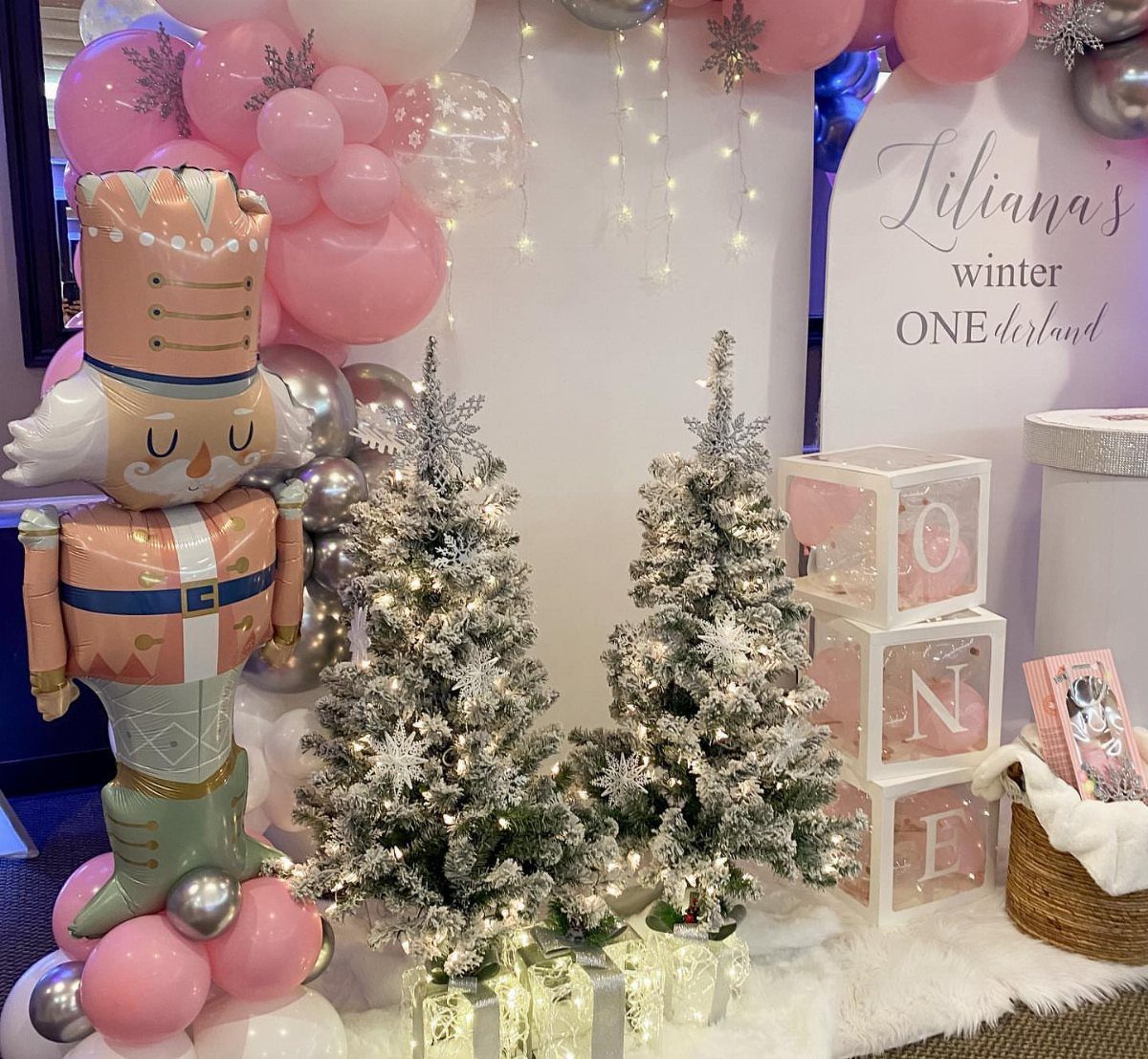 Winter wonderland party setup with nutcracker balloon, frosted trees, and pink balloons.