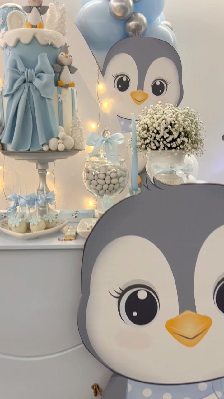 Party dessert table with a blue cake and cute cartoon penguin decorations.