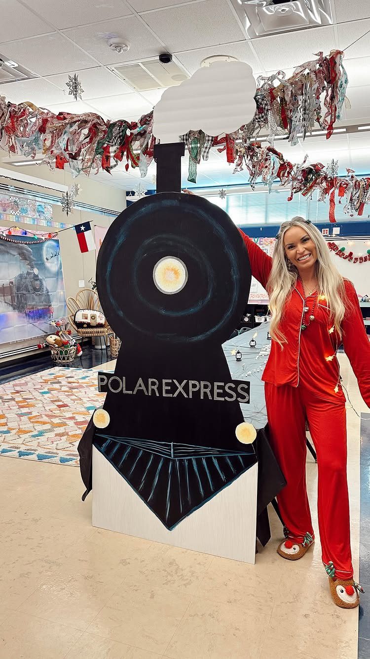 Woman in red pajamas posing beside a Polar Express train cutout in decorated room.