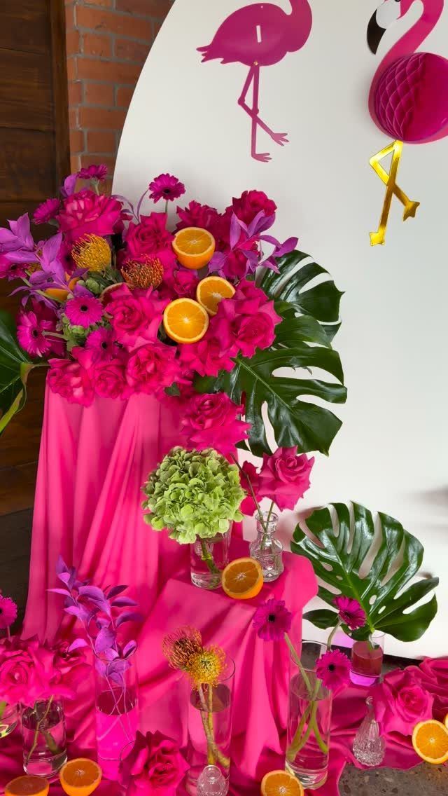 Pink flamingo party decorations with vibrant flowers, tropical leaves, and pink fabric draping.