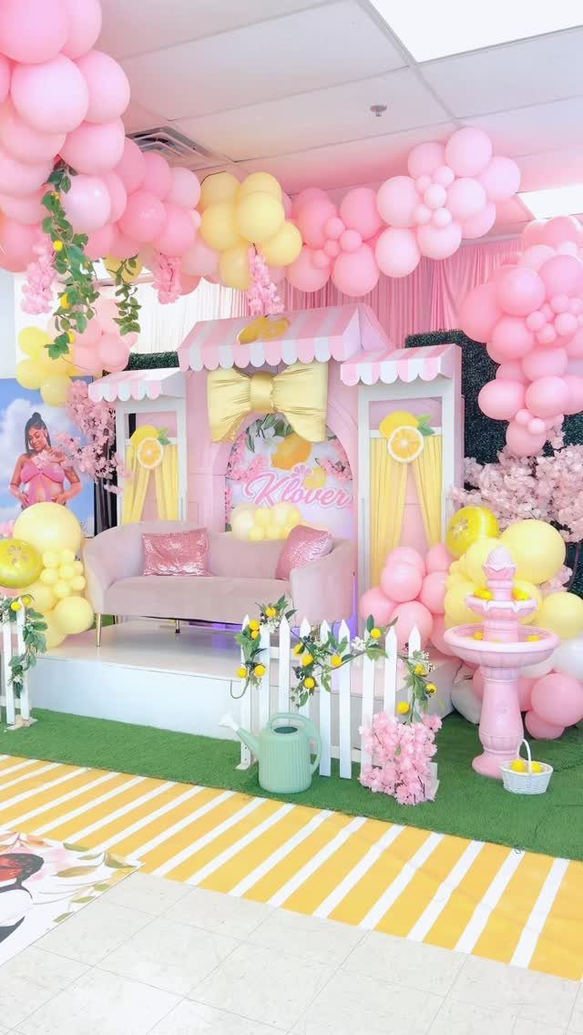 Pink and yellow lemonade stand party setup with balloons, sofa, and picket fence.