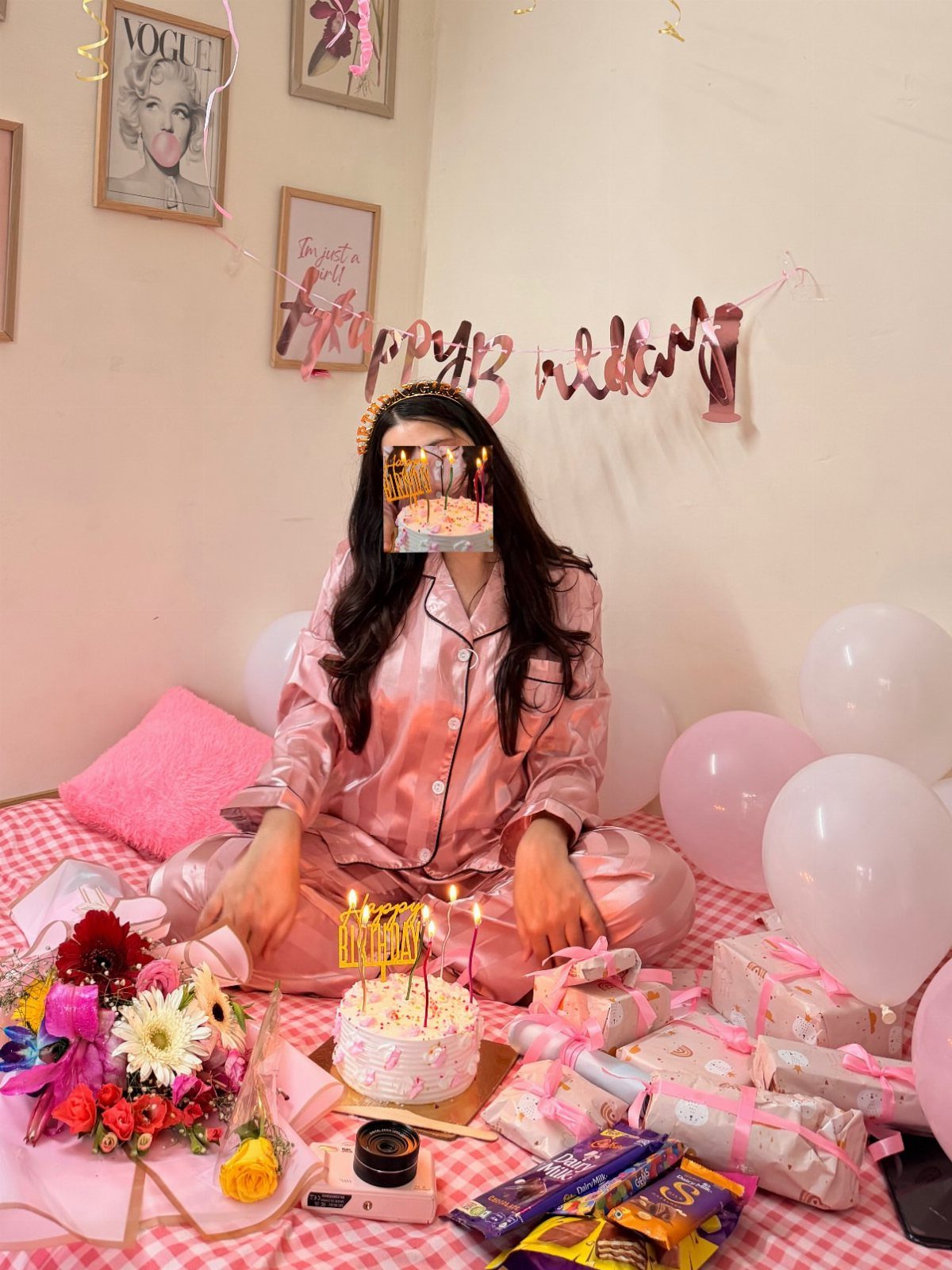 Woman in pink satin pajamas celebrating birthday with cake, balloons, and gifts.