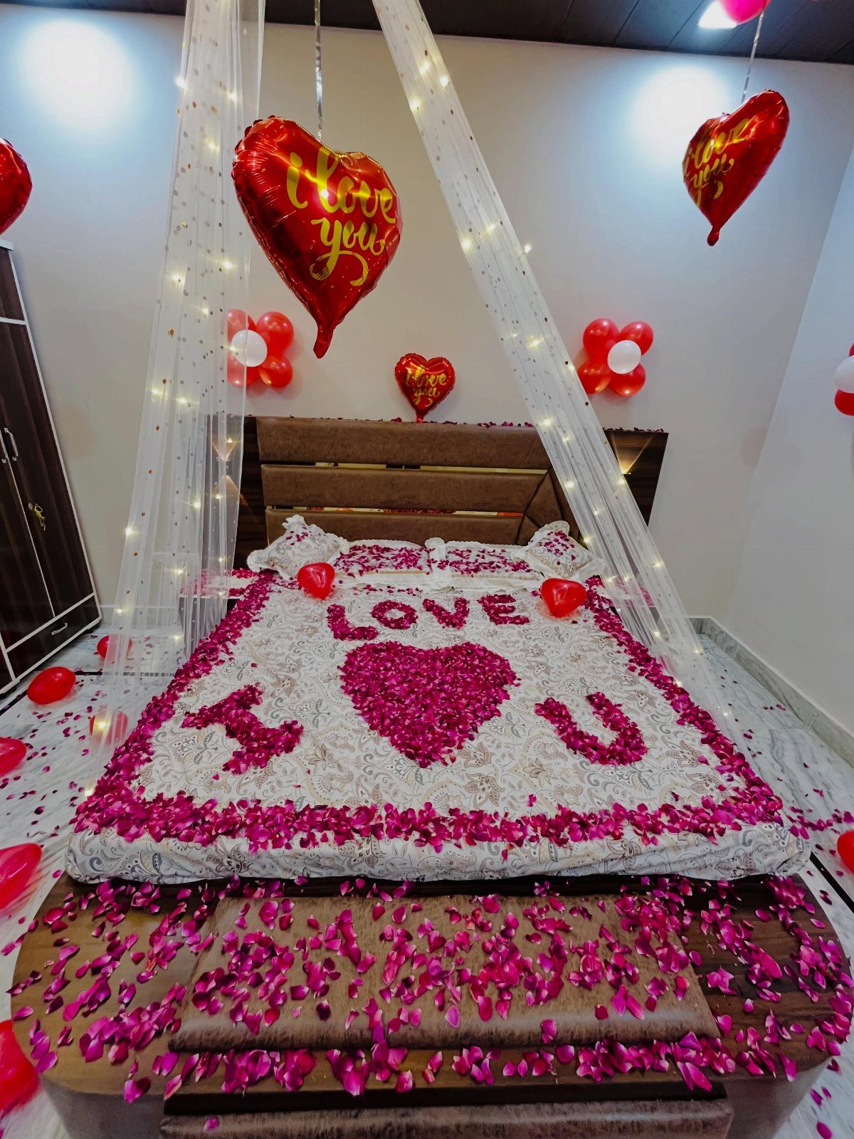 Bedroom decorated with red heart balloons and pink flower petals on the bed