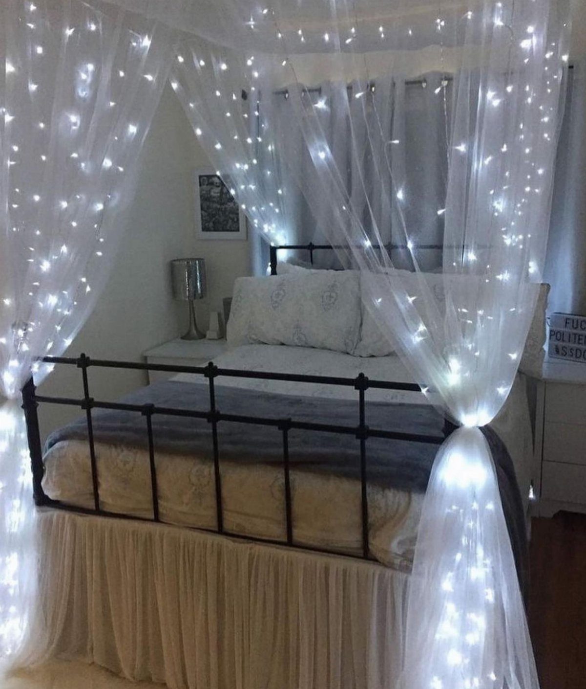 Bed with black metal frame and white canopy draped with glowing fairy lights