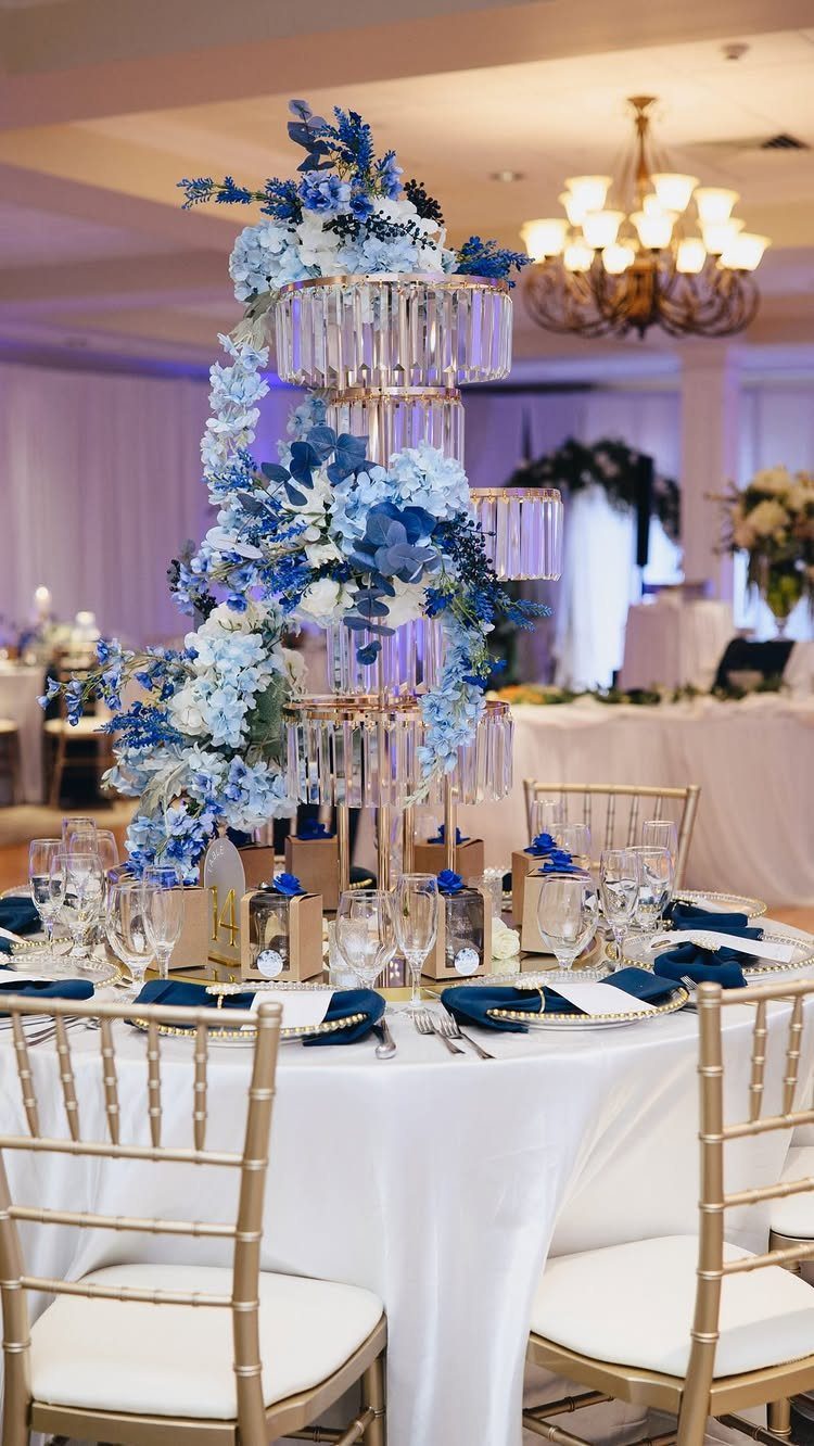 Tall tiered gold centerpiece with blue flowers and crystals on a wedding table.