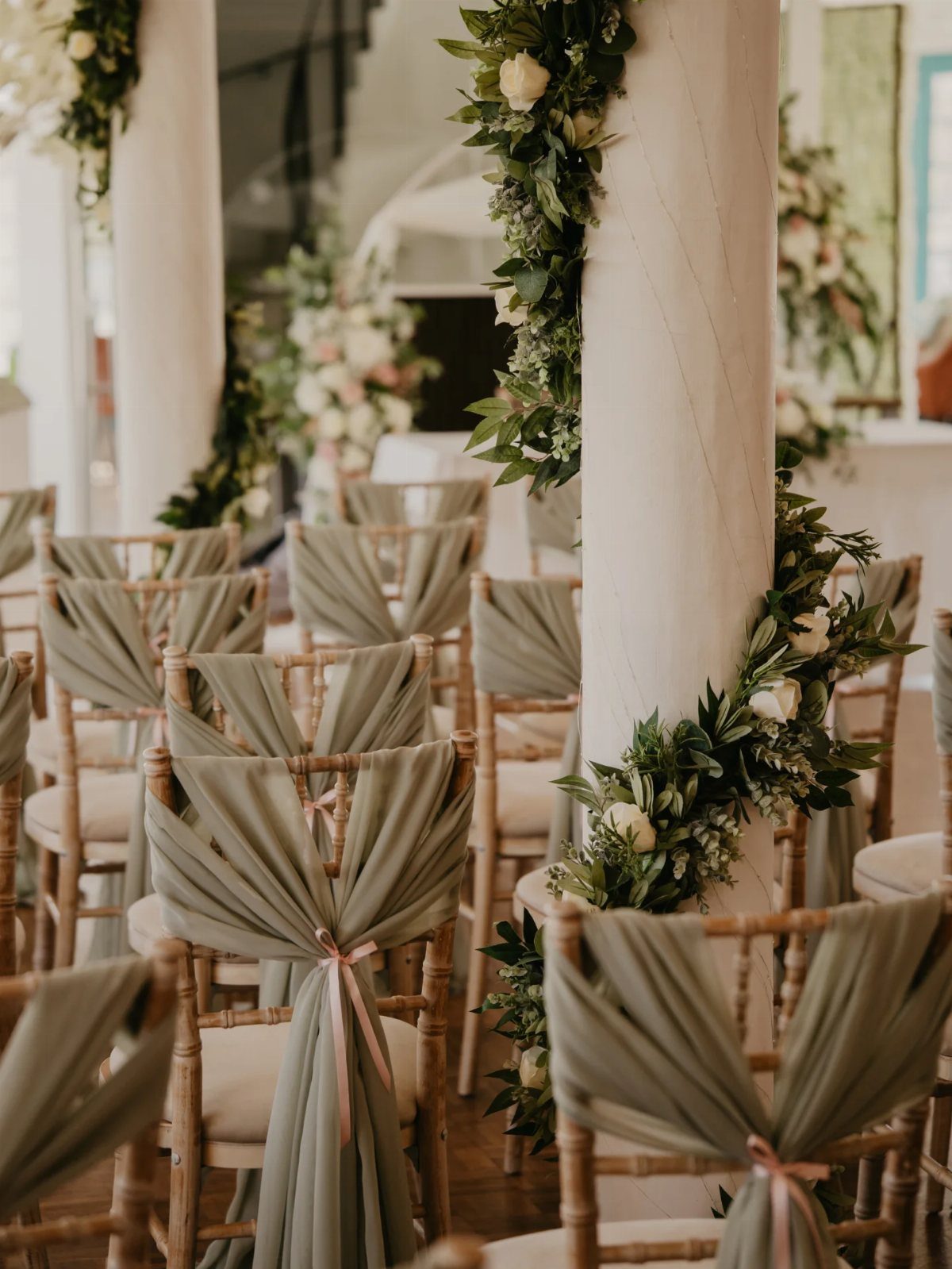 Wooden wedding chairs decorated with sage green fabric drapes and pink ribbons.