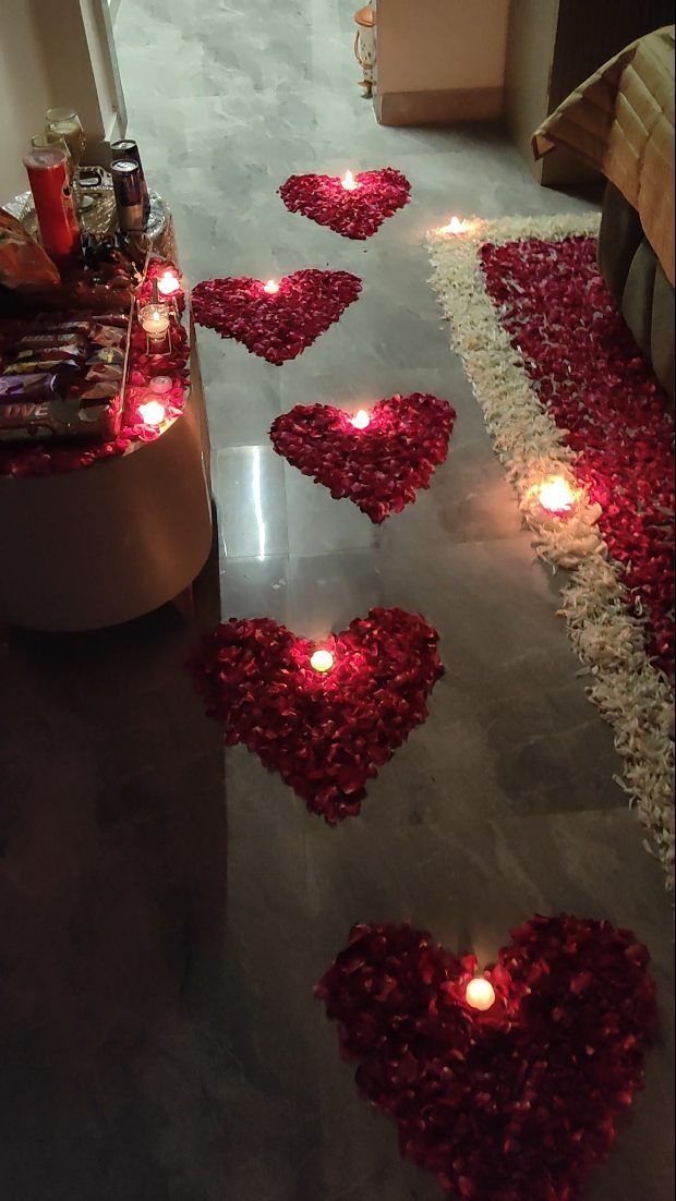 Red rose petal hearts with lit candles on a grey tiled floor
