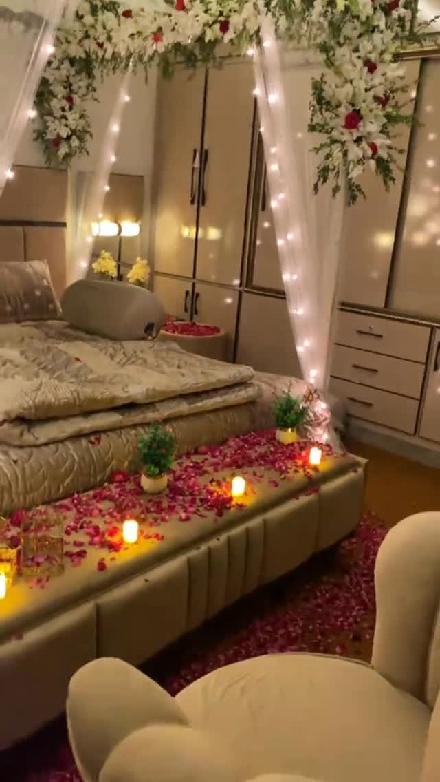 Bedroom decorated with red rose petals, white floral garlands, and warm string lights.