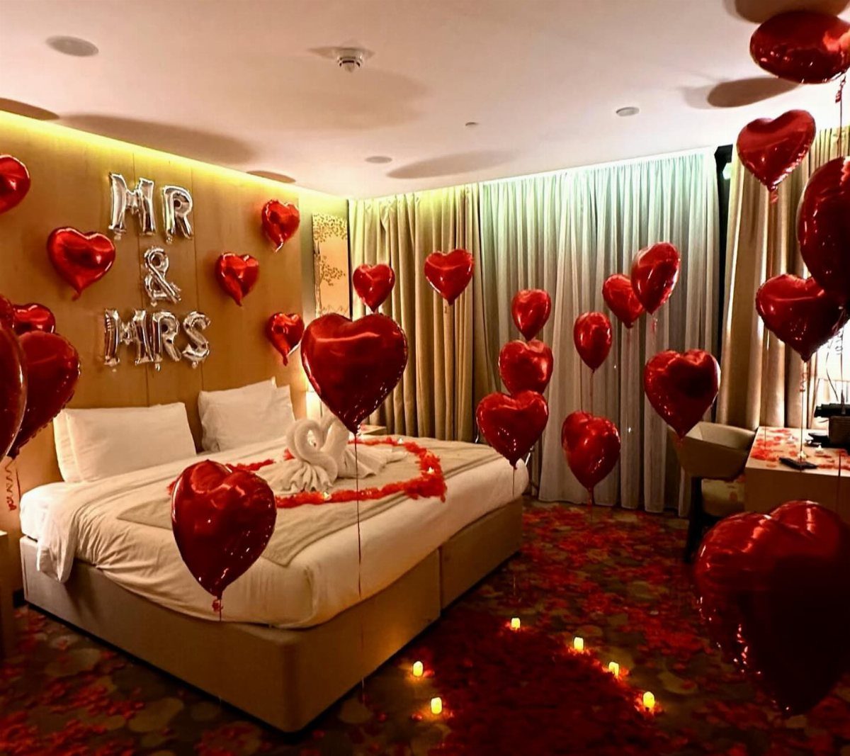 Bedroom decorated with red heart balloons, rose petals on bed, and MR & MRS balloons.