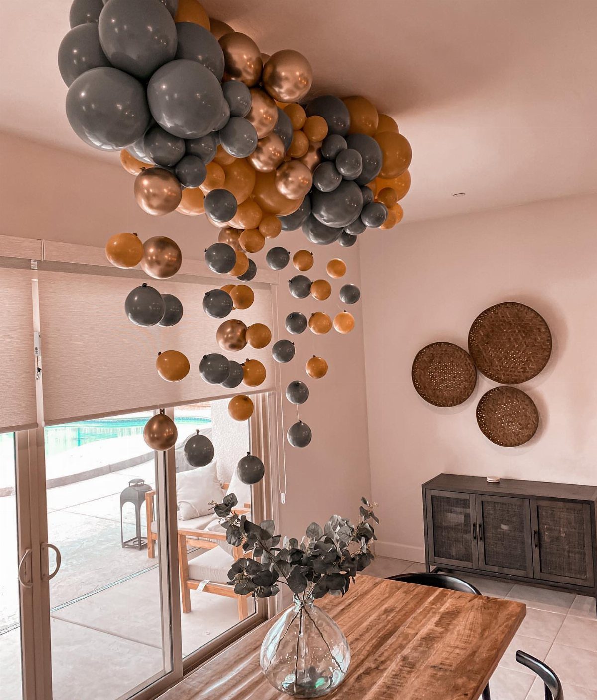 Grey and gold balloons cascading from the ceiling over a wooden dining table