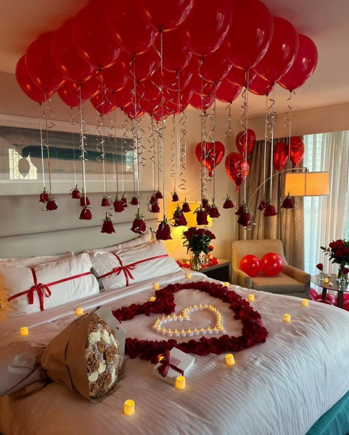 Red balloons on a ceiling with roses hanging over a heart-shaped rose petal bed.