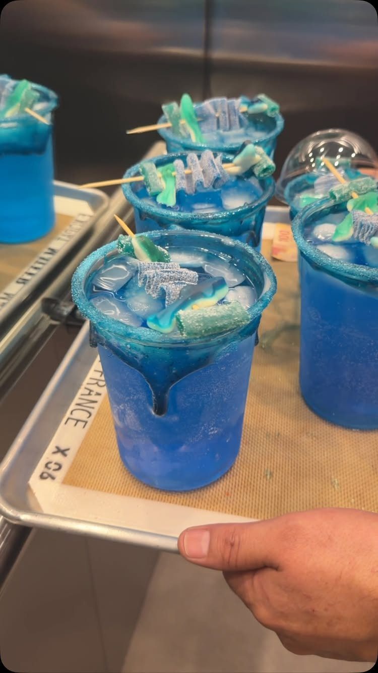 Blue frozen drinks topped with gummy sharks on picks on a metal tray
