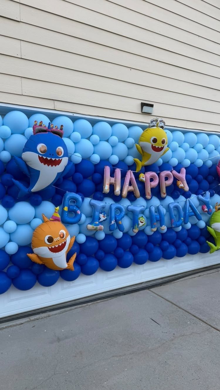 Shark-shaped foil balloons and birthday letters set against a blue balloon wall.
