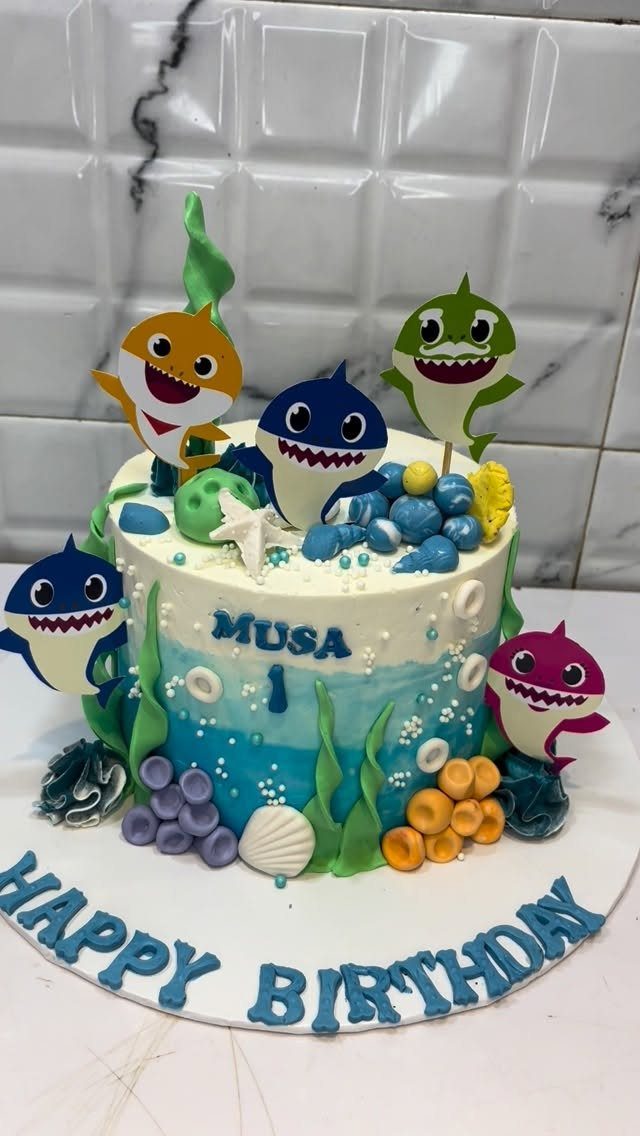 Shark themed birthday cake with blue ocean frosting and cartoon shark toppers.