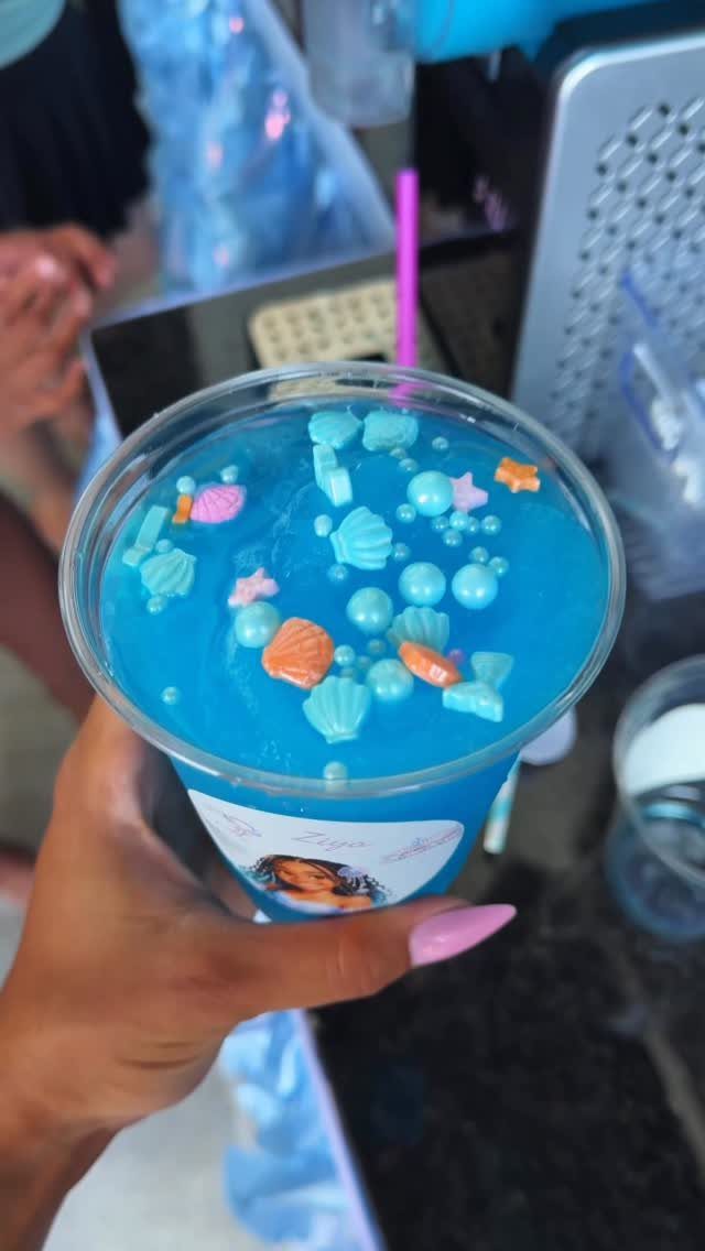 Blue drink in a plastic cup topped with seashell and starfish candies.