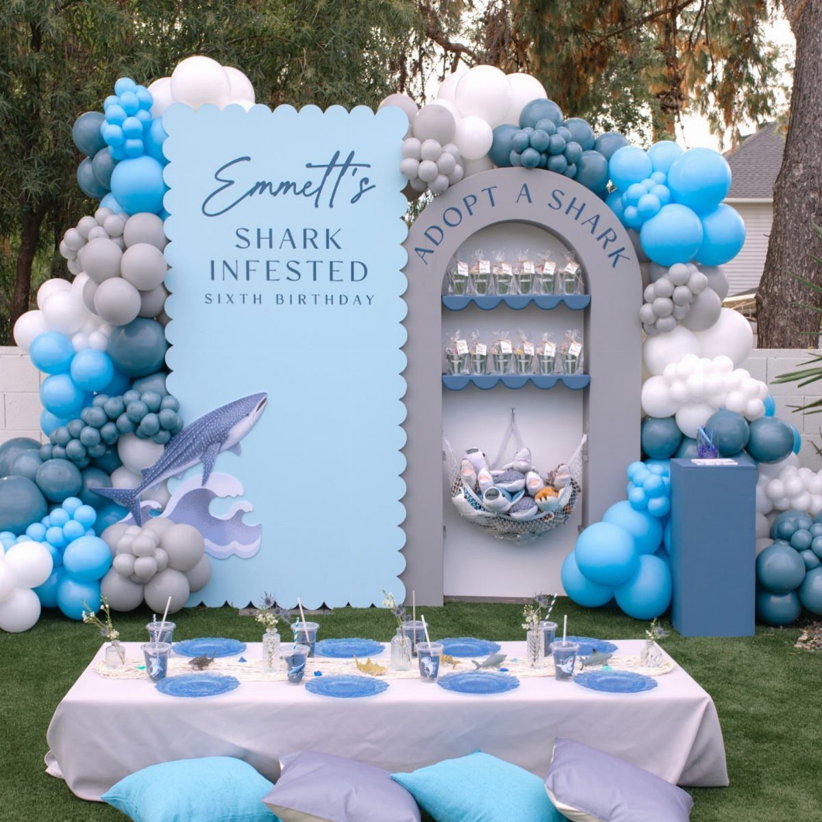 Shark themed birthday party setup with blue balloon arches and a themed backdrop.