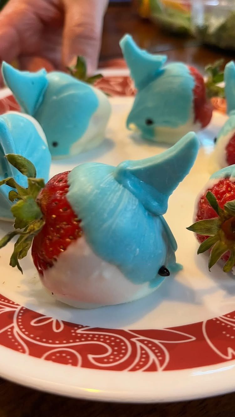 Shark-shaped chocolate covered strawberries on a red and white patterned plate.