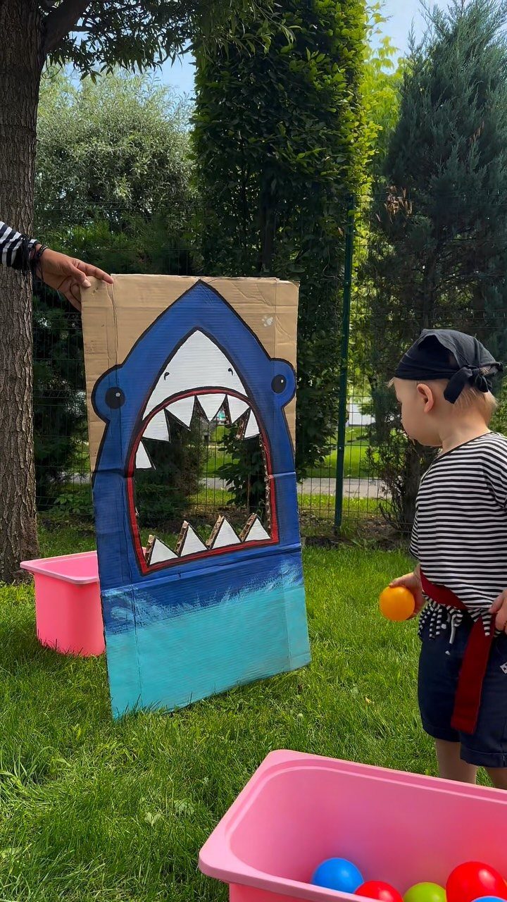Child playing a shark toss game with a cardboard shark and colorful balls.