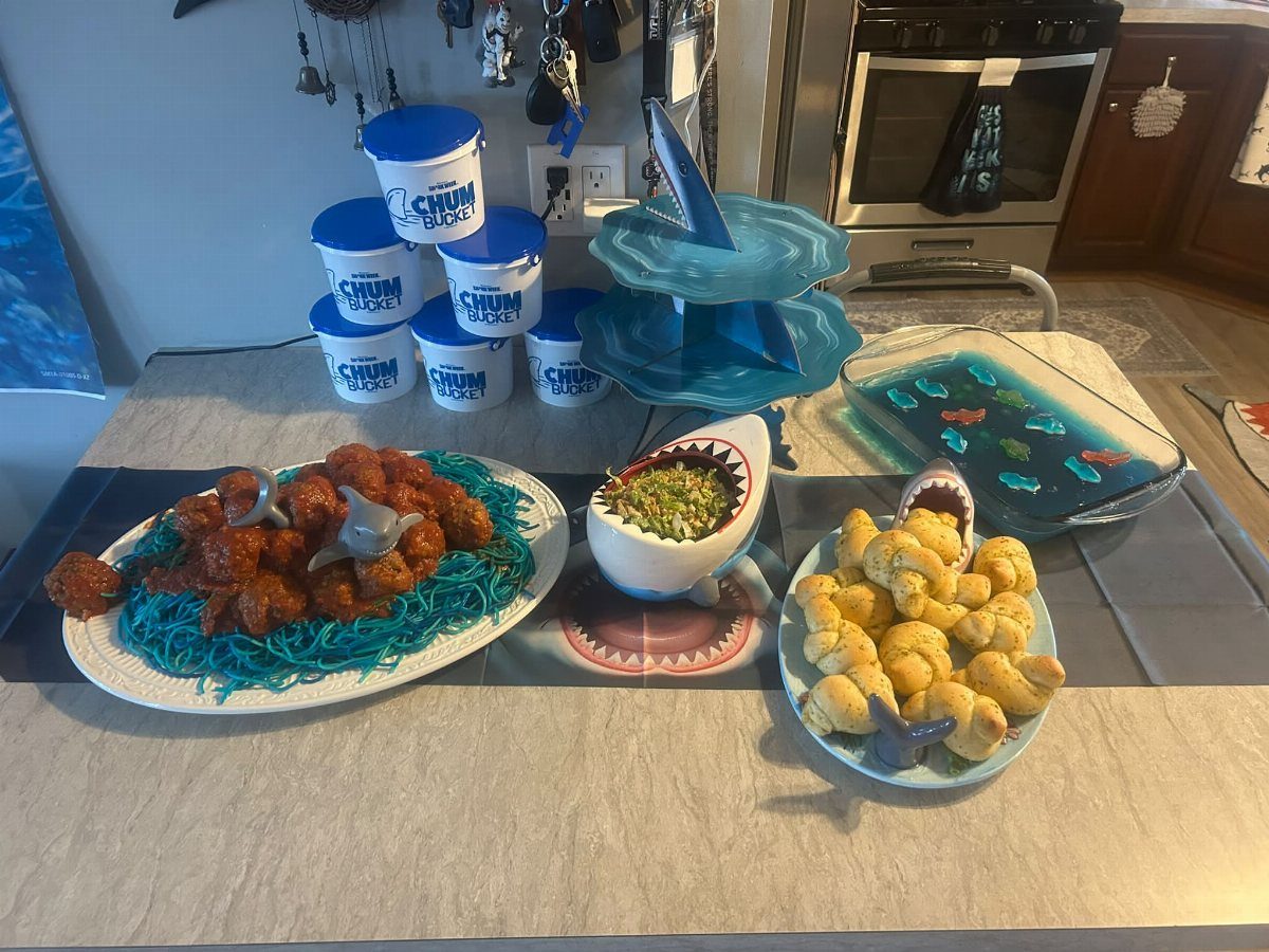 Shark themed party snacks including fried chicken, popcorn, and pastries in shark bowls.