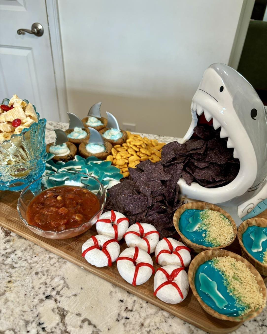 Shark-themed party food spread with a shark bowl, blue dips, and red-striped treats.