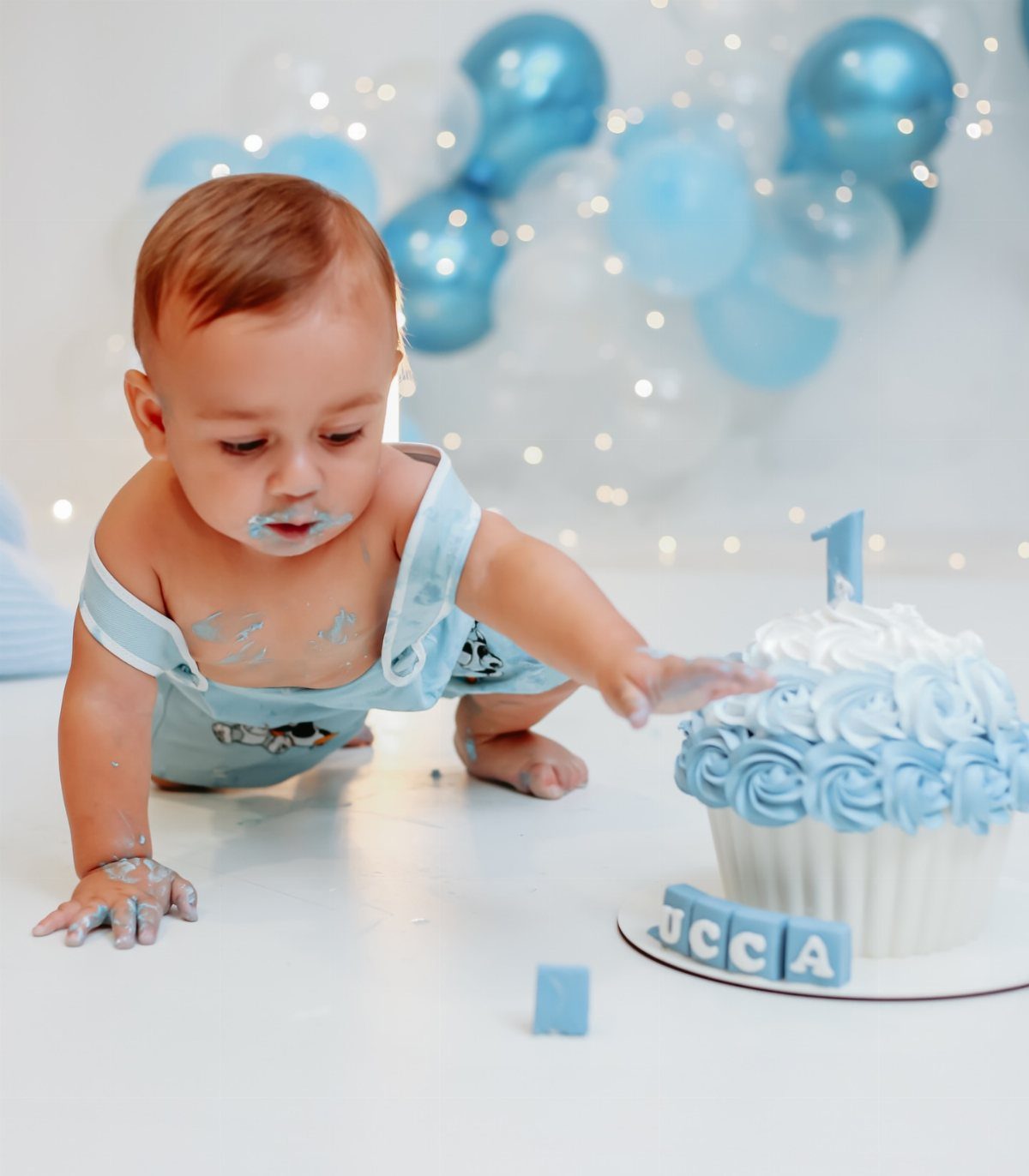 Baby boy crawling toward a blue and white frosted smash cake with candle