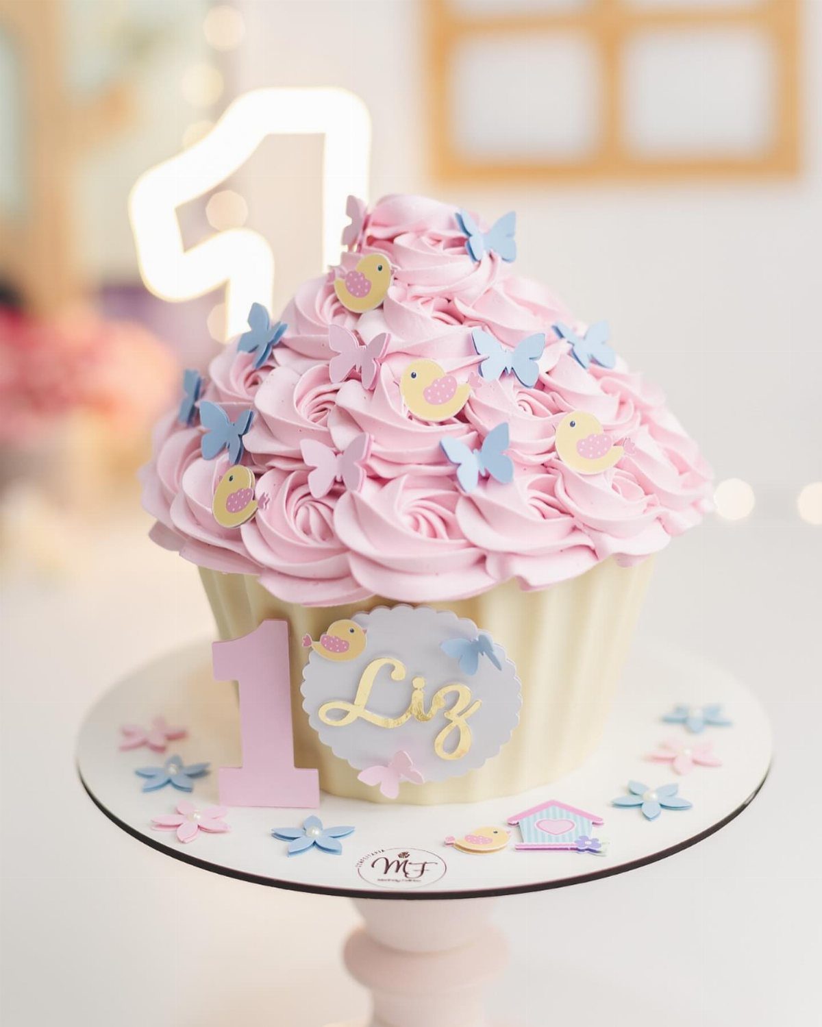Cupcake-shaped cake with pink frosting decorated with small blue and pink butterflies.