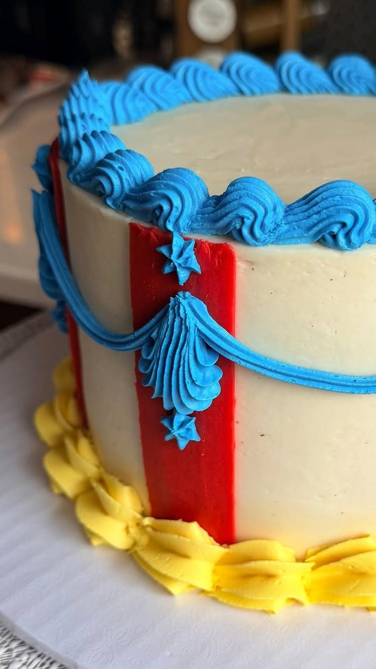 White cake with red stripes, blue piped swirls, and yellow frosting base.