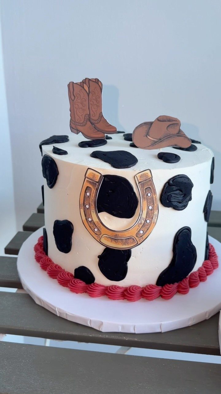 Cowboy themed cake with cow print, a horseshoe, boots, and a hat.