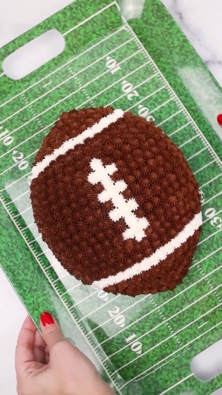 Football shaped cake with brown and white frosting on a football field tray
