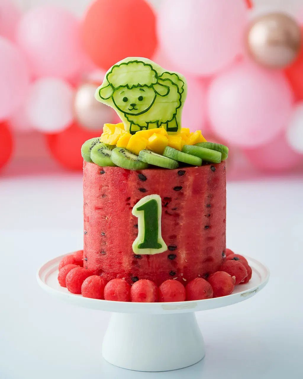 Watermelon carved into a cake shape topped with kiwi, mango, and a sheep topper.