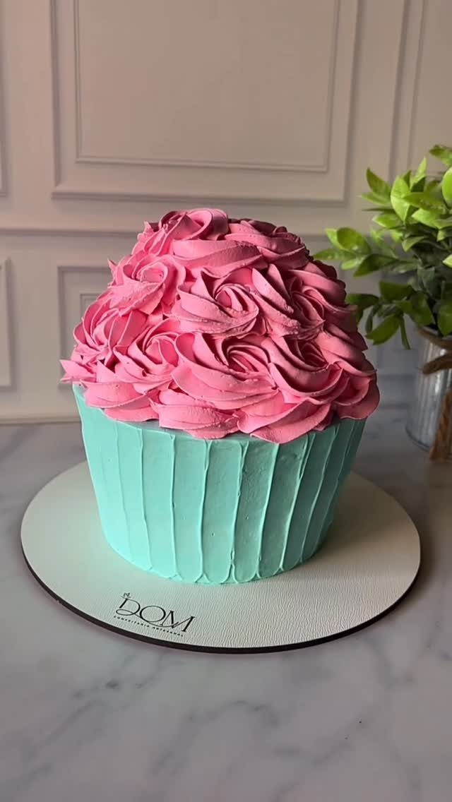Cupcake-shaped cake with turquoise frosting base and pink rose-swirl frosting on top.