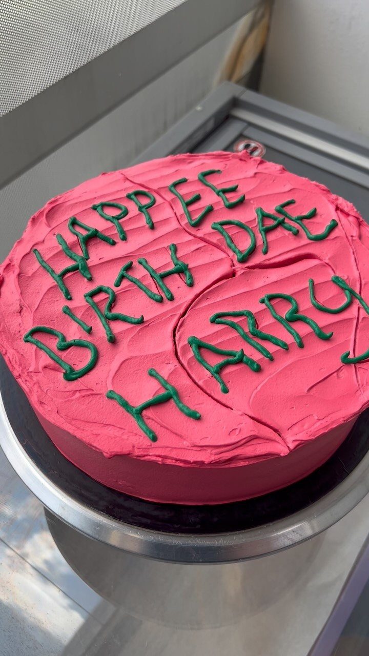 Pink frosted cake with green icing reading Happee Birth Dae Harry on silver stand