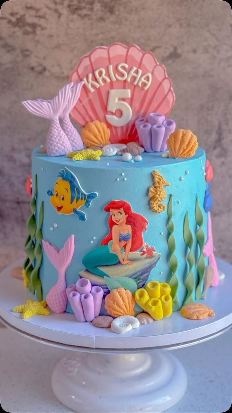 Blue mermaid themed cake with sea creatures and a pink shell topper.