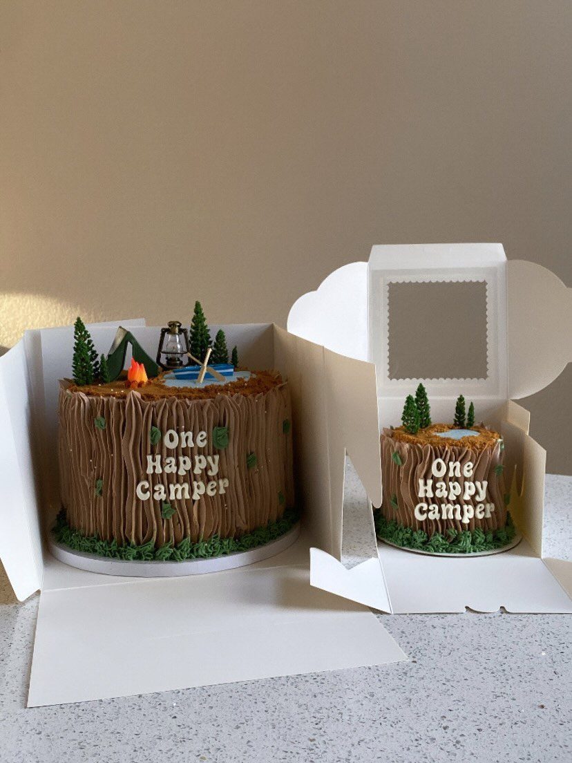 Tree trunk cakes with miniature camping decorations and One Happy Camper text.
