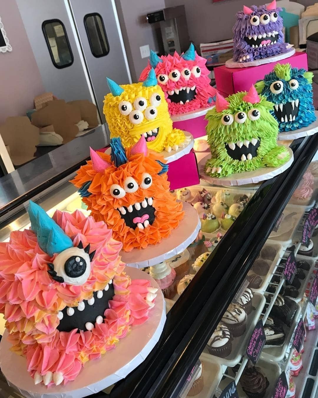 Colorful monster cakes with frosting fur and googly eyes on a bakery counter