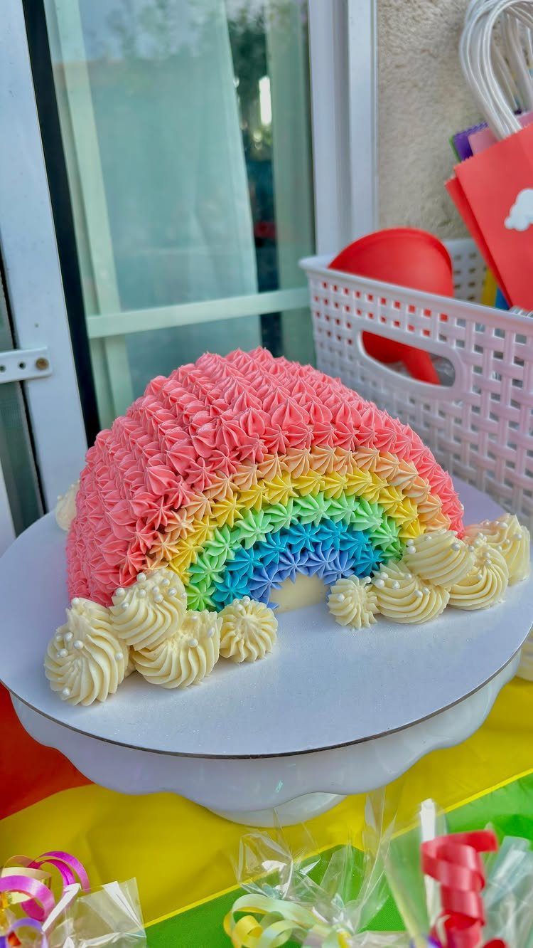 Rainbow shaped cake with colorful piped frosting stars and white frosting clouds.