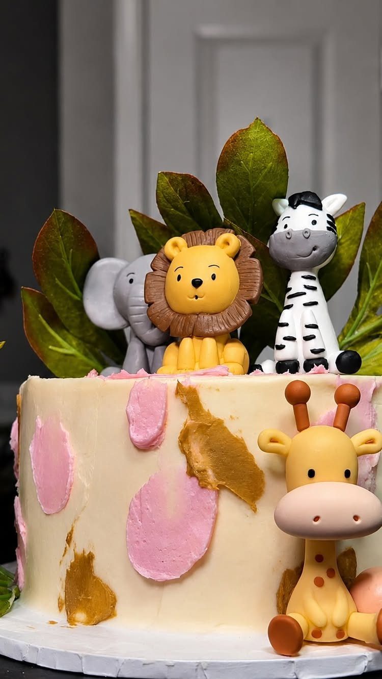 White frosted cake with animal figurines and pink and gold decorative smears.