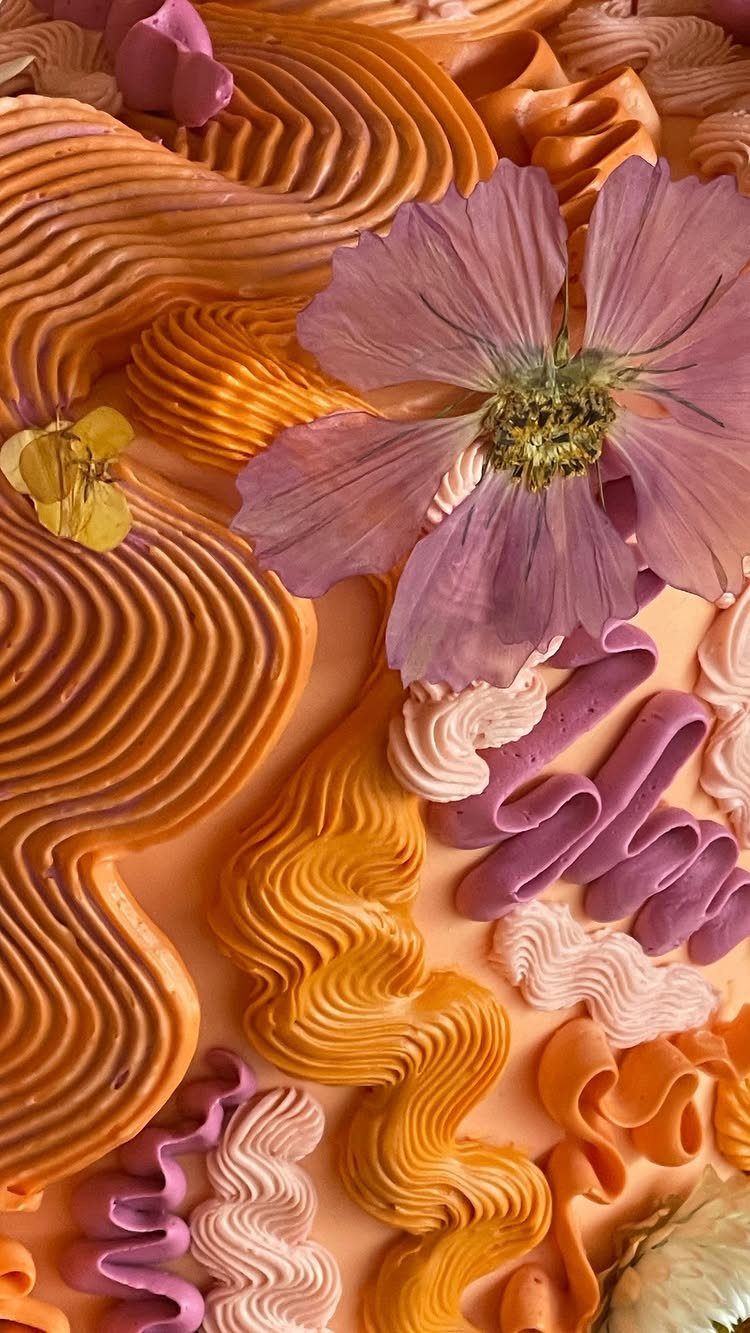 Colorful frosting squiggles in orange and purple with a purple flower on cake.
