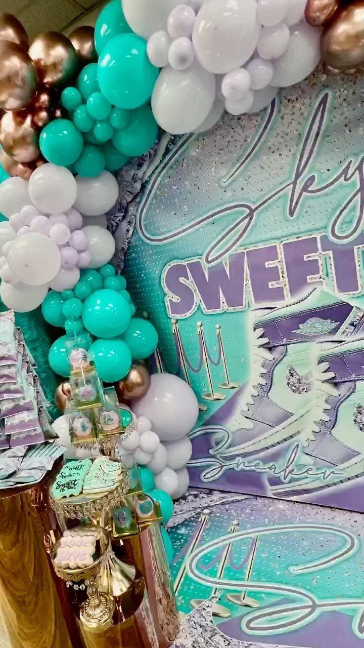 Teal and white balloon arch next to a sneaker-themed party backdrop and desserts.