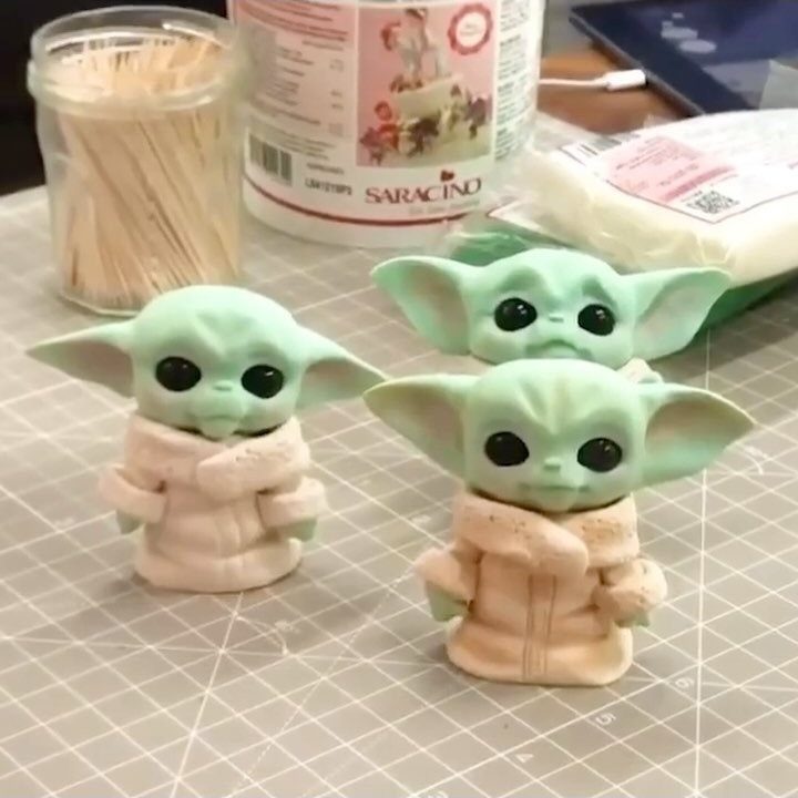 Three small green fondant Grogu figures on a grey gridded cutting mat.