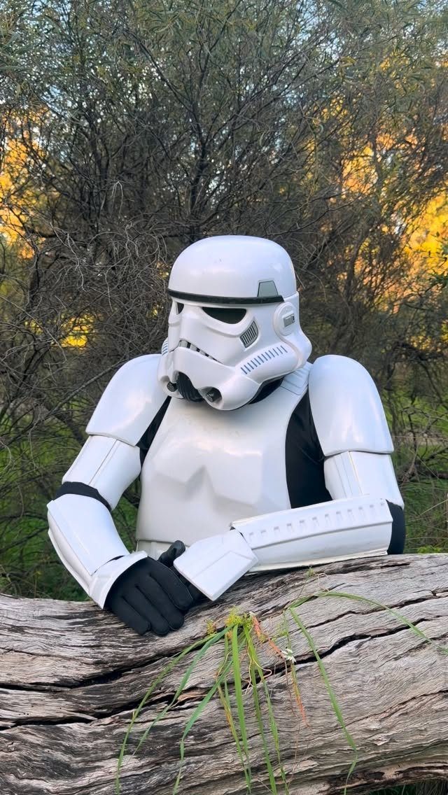 Stormtrooper in full white armor leaning on a log in a wooded area