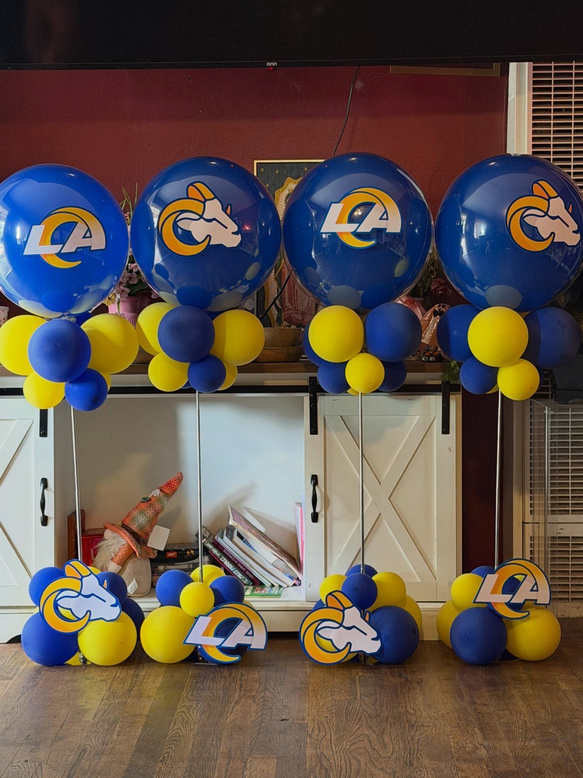 Blue and yellow Los Angeles Rams balloon arrangements standing on a wooden floor.