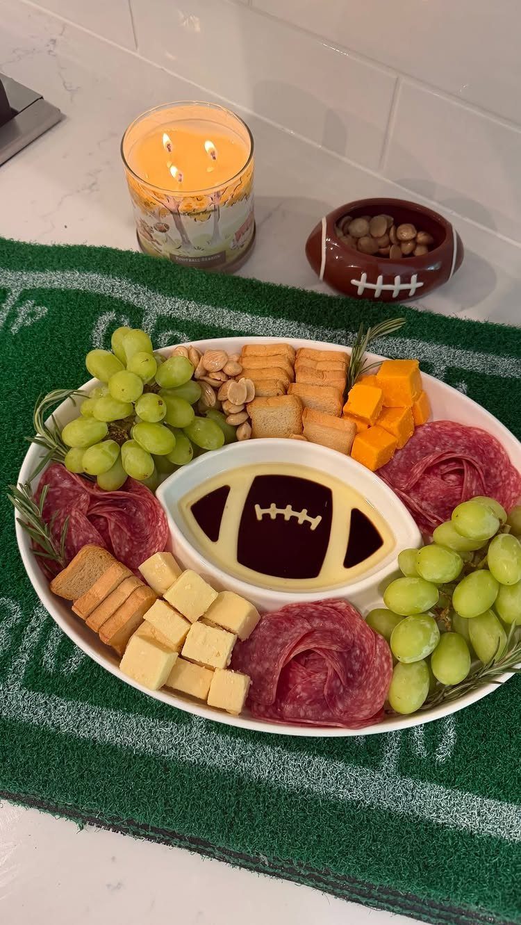 Charcuterie platter with football-shaped dip on a green grass-textured table runner.