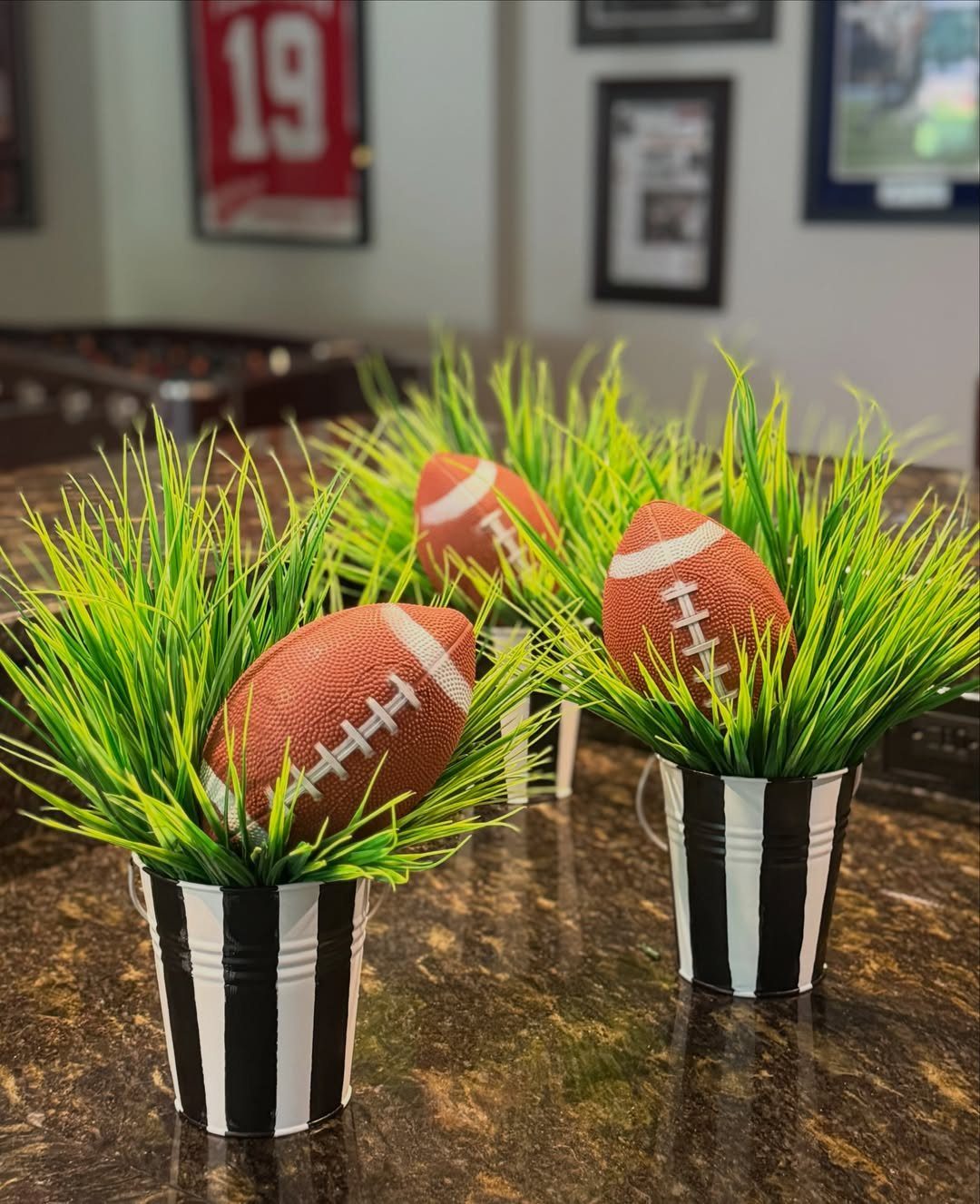 Three striped buckets with green grass and footballs as table centerpieces.
