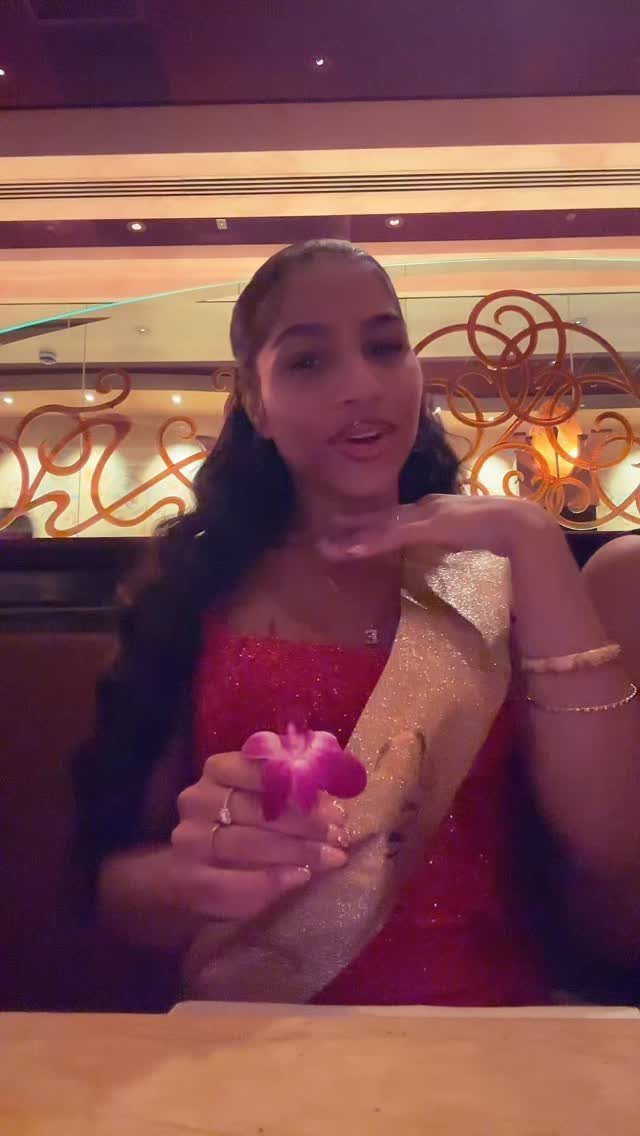 Young woman in red sequined dress and gold sash holding a pink flower