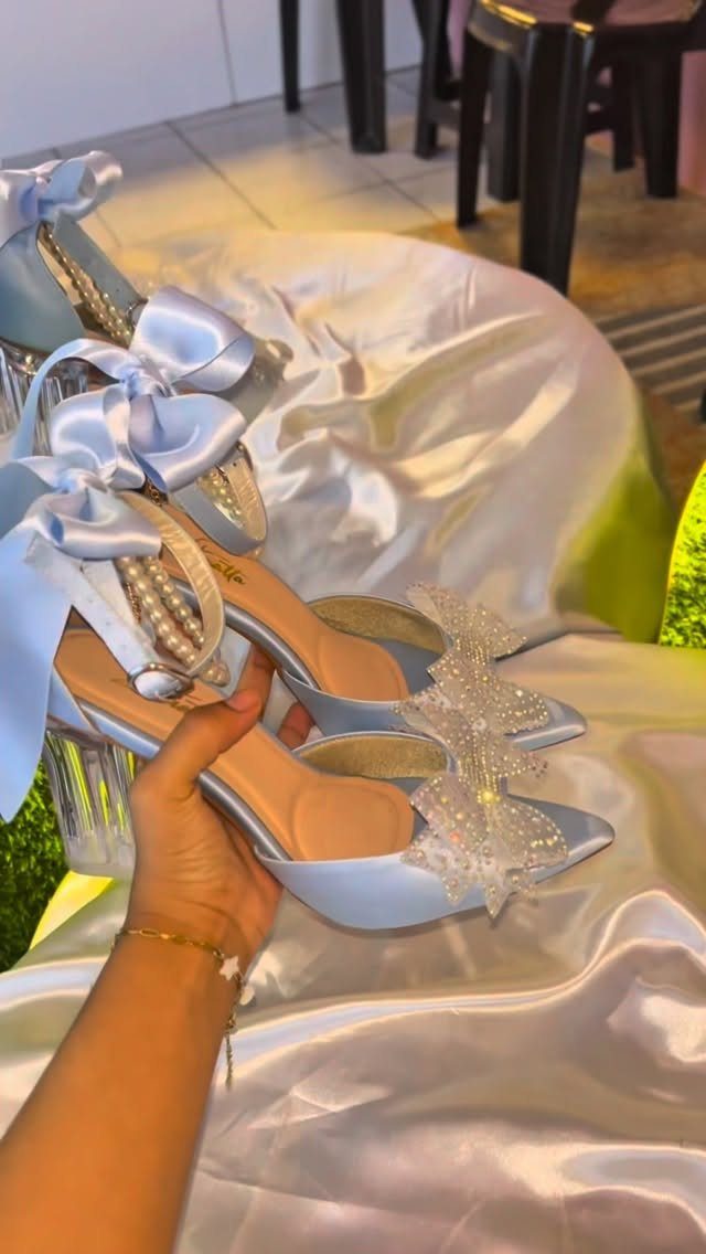 Light blue high-heeled shoes with pearl straps and bows on white satin fabric.