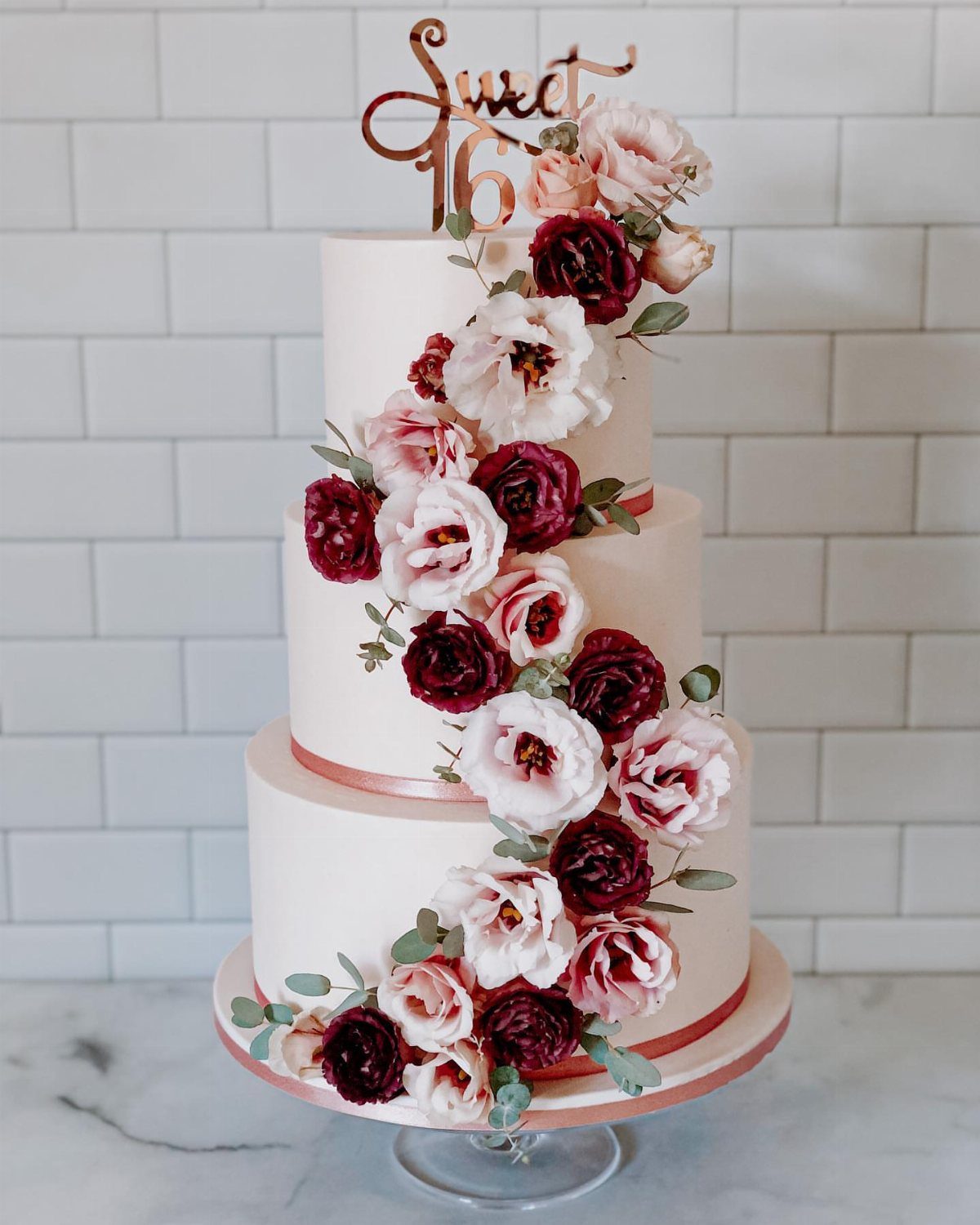 Three-tier white cake with cascading red and pink flowers and Sweet 16 topper.